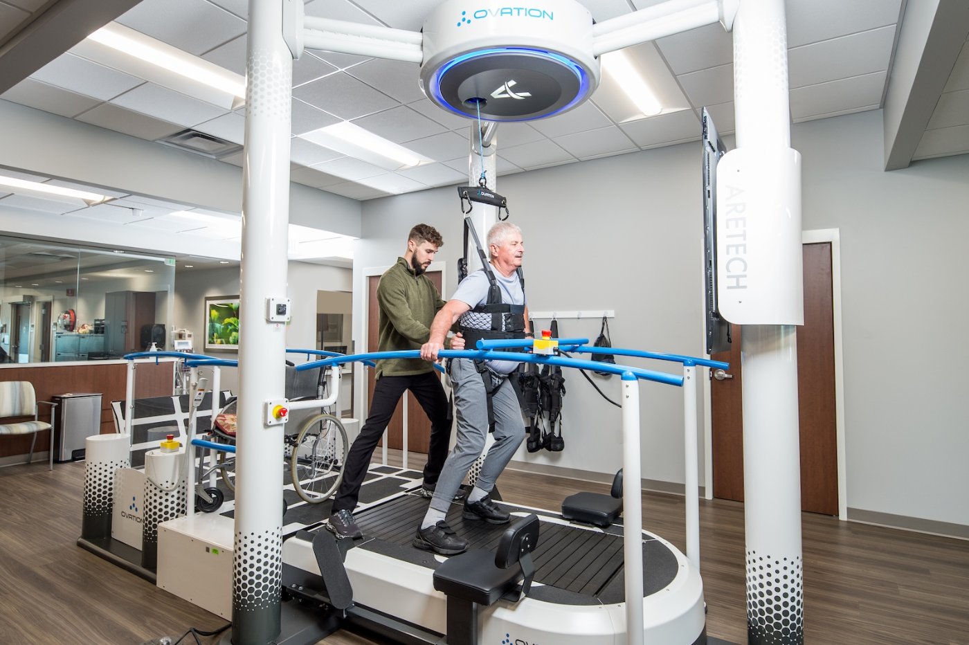 Therapist assisting a patient walking on the Ovation treadmill with dynamic body-weight support
