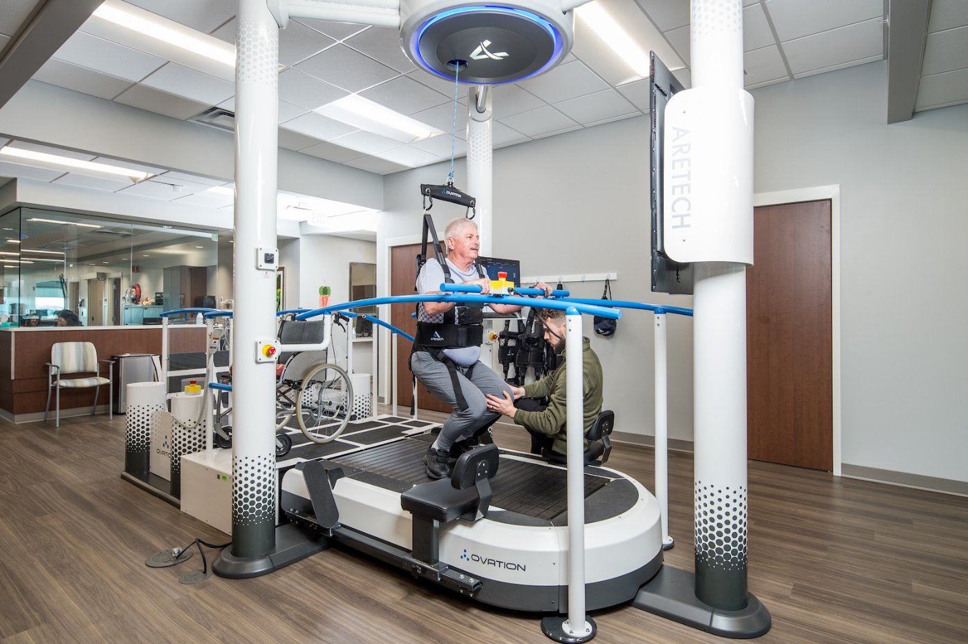 Patient in the Ovation harness with a therapist guiding range-limited fall protection at the treadmill