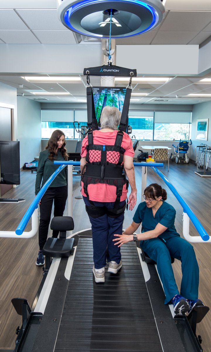 Patient walking on the Ovation slat-belt treadmill with two therapists assisting
