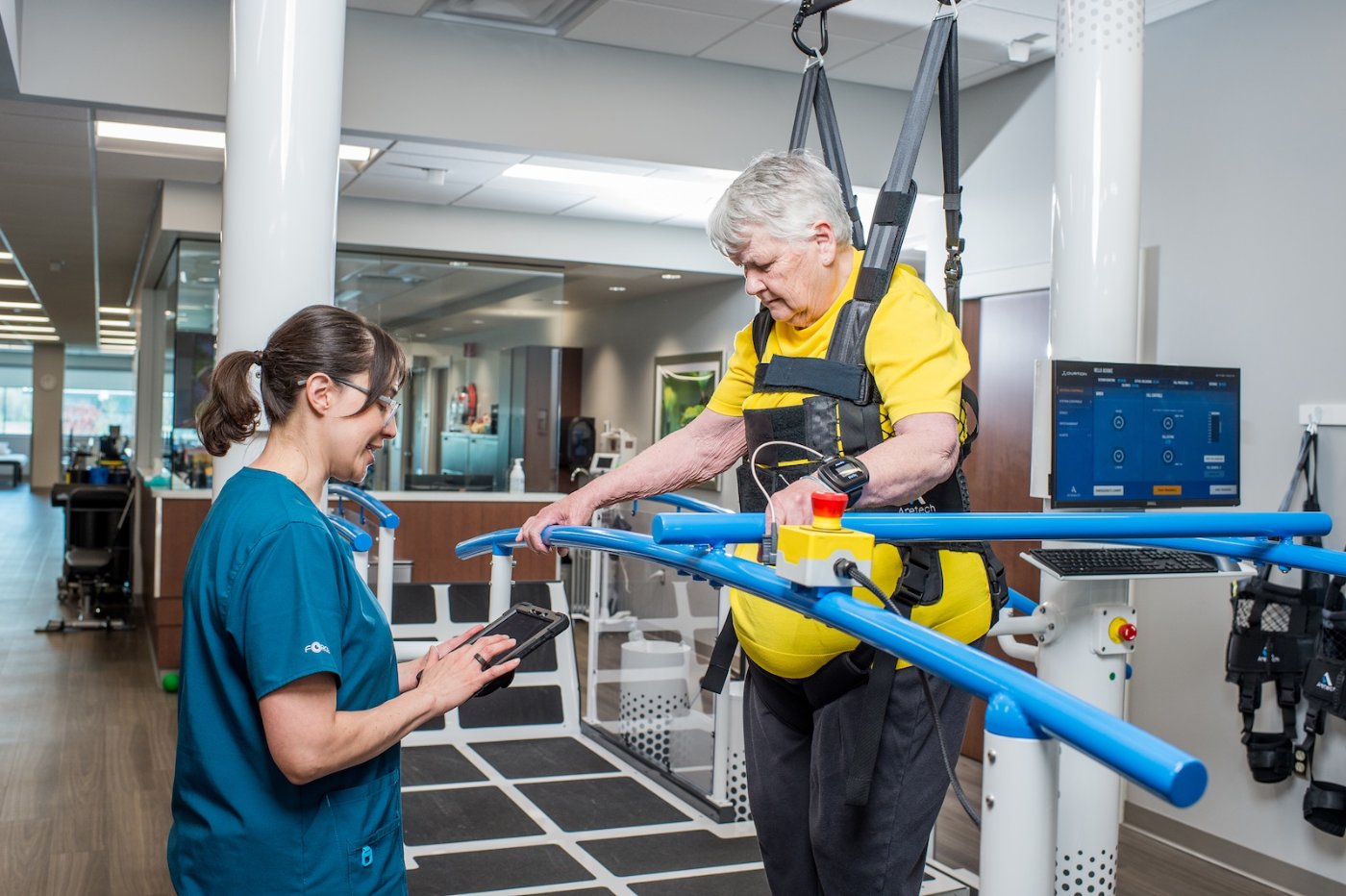 Therapist adjusting Ovation settings on a wireless tablet beside a patient in the harness