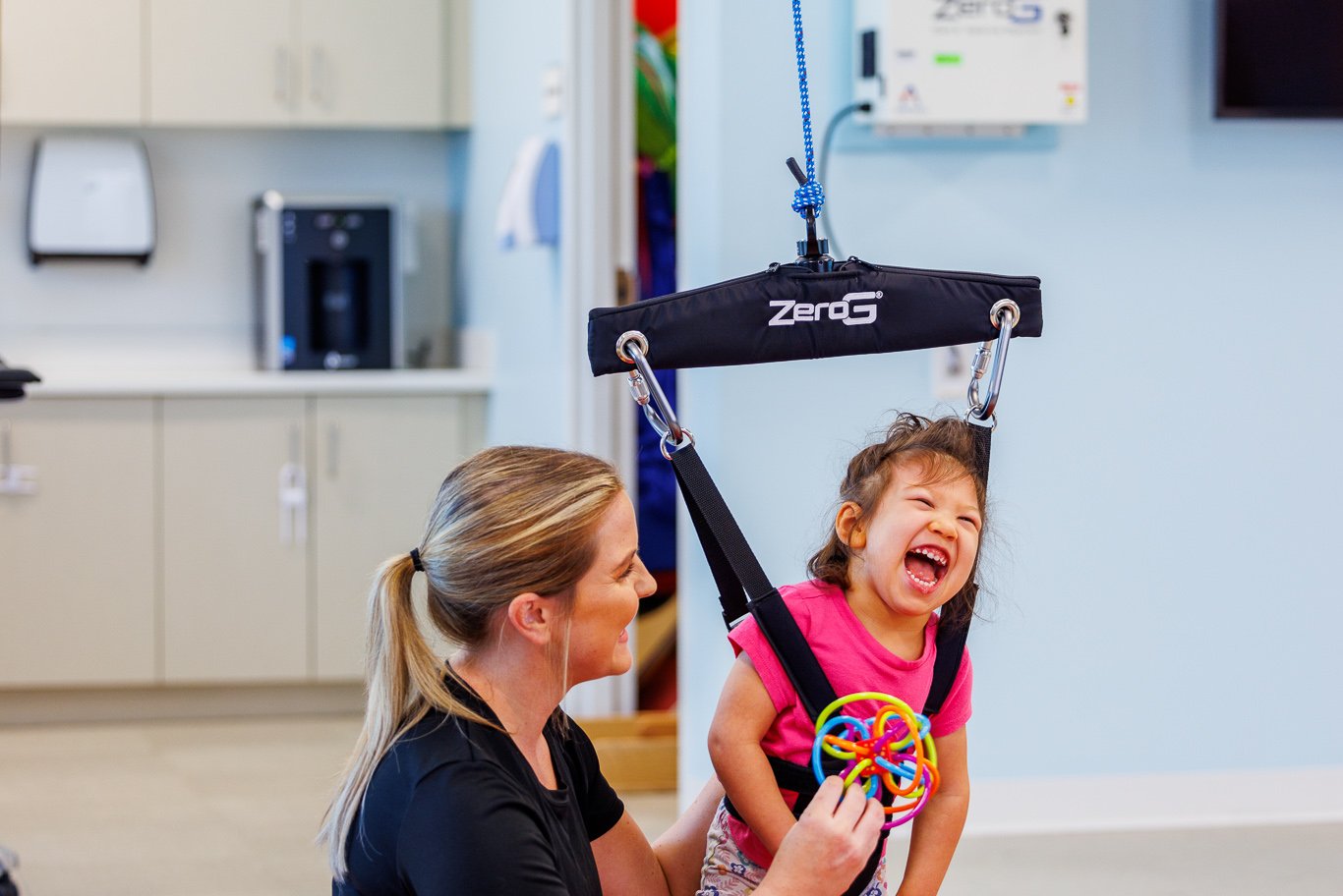 Child laughing in a ZeroG sling during pediatric therapy