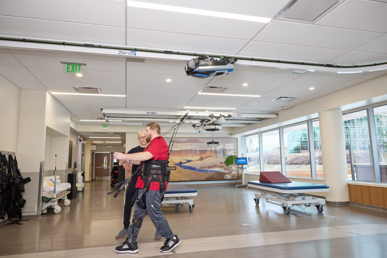 Patient walking while a clinician guides reactive balance from behind in a ZeroG harness